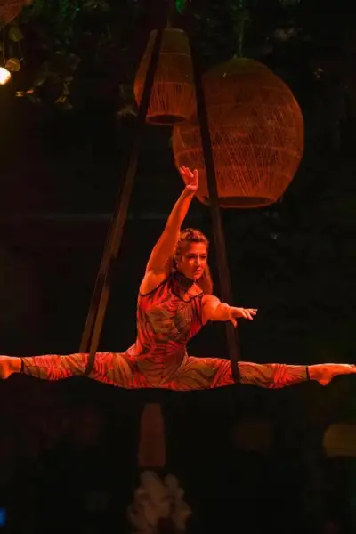 Aerial fabric artist in a colorful costume performing a full split midair under wicker lanterns at Nouba, Marrakech