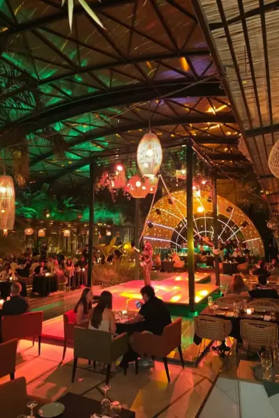 Interior view of Nouba restaurant in Marrakech, showing dinner tables, a runway-style stage, glass roof, and lush ambient lighting during the live show