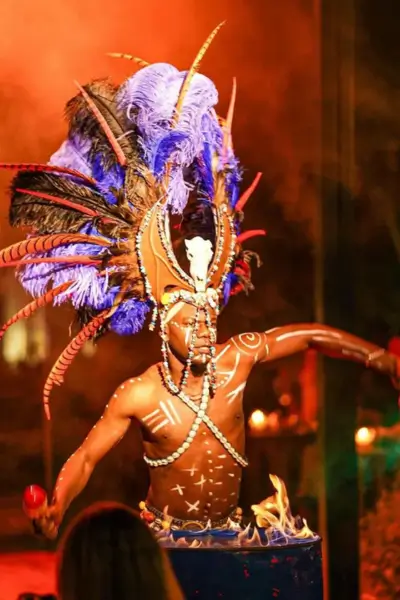 Tribal-inspired dancer wearing an ornate feathered headdress performing by a flaming drum at Nouba restaurant, Marrakech