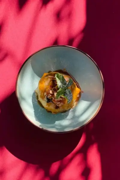 Citrus pastry dessert garnished with almond slices and fresh mint in a blue bowl on a red table at Terrasse des Épices, Marrakech