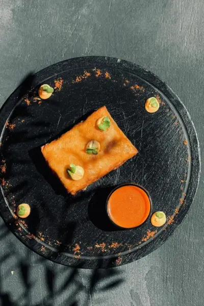 Golden fried briouat served with a spicy dipping sauce and microgreens on a black slate plate at Terrasse des Épices, Marrakech