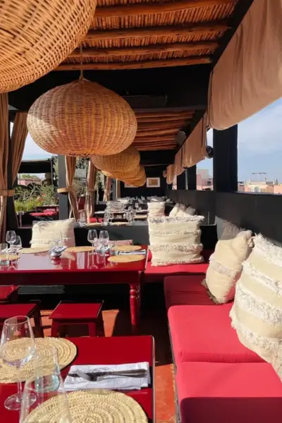 Rooftop dining lounge at Terrasse des Épices in Marrakech, featuring red cushioned benches and woven rattan lanterns under a reed canopy