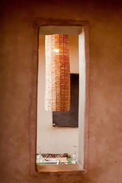 Wicker pendant lamp framed by a narrow plaster window opening, overlooking the dining area at Terrasse des Épices, Marrakech